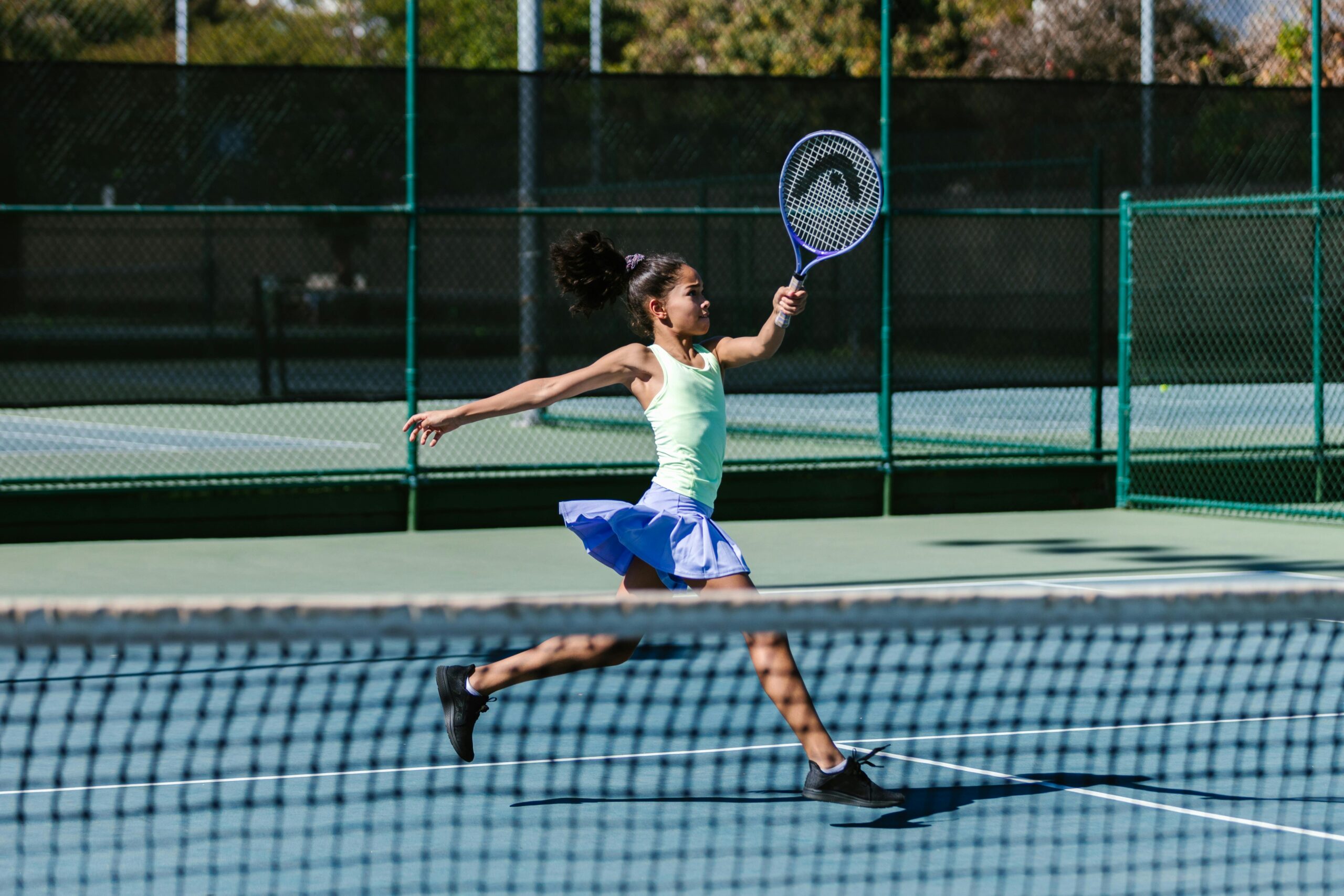 Image of young girl playing tennis in a periwinkle blue skirt and seafoam green tank top.